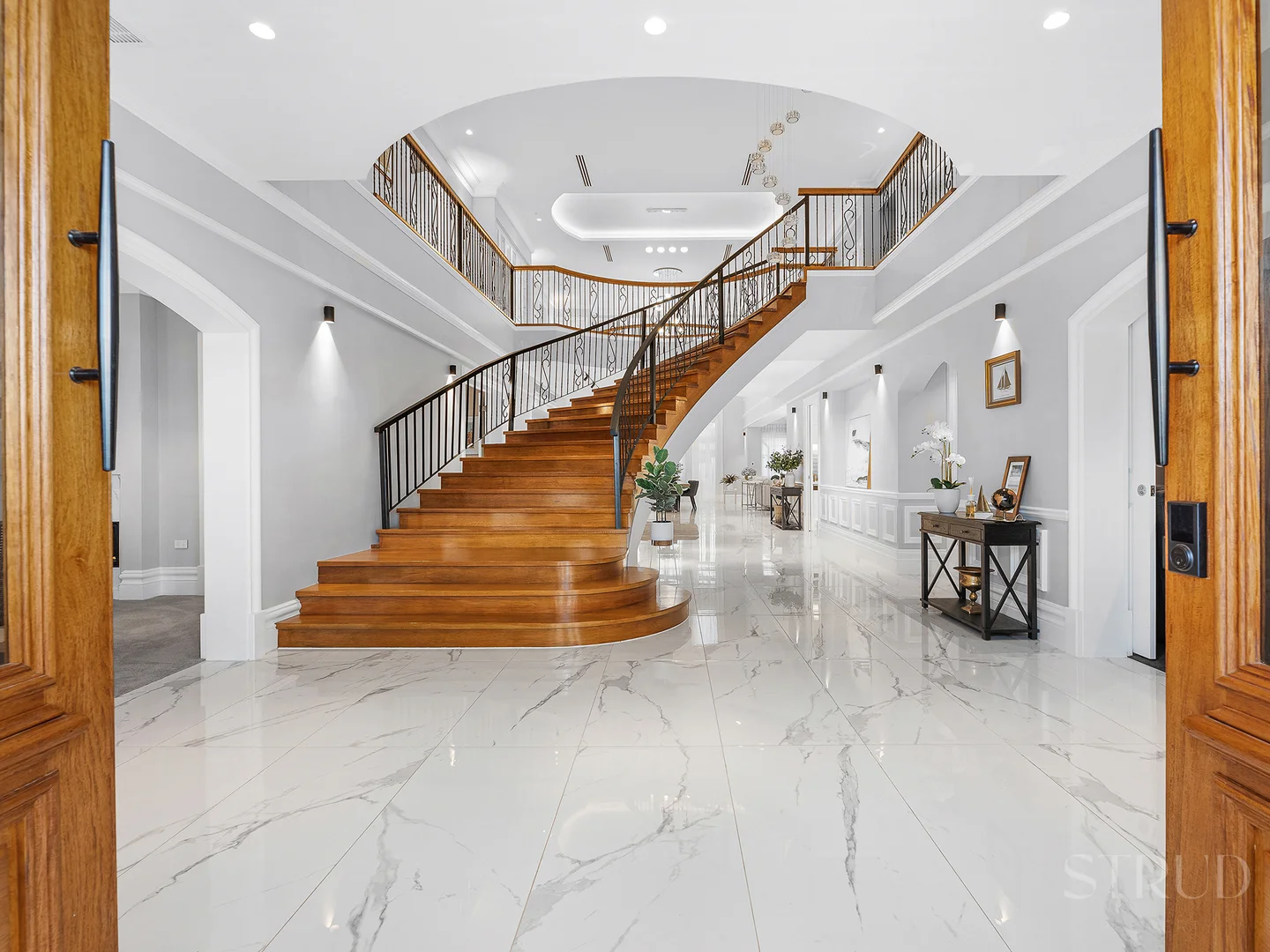 Grand curved timber staircase with wrought iron balustrade in marble foyer