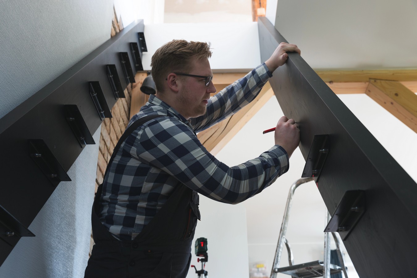 Installer fitting steel stringer brackets during staircase construction to building code standards