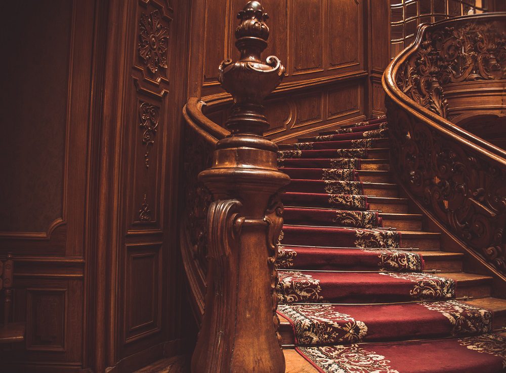 Ornate carved timber staircase with decorative balusters and red carpet runner