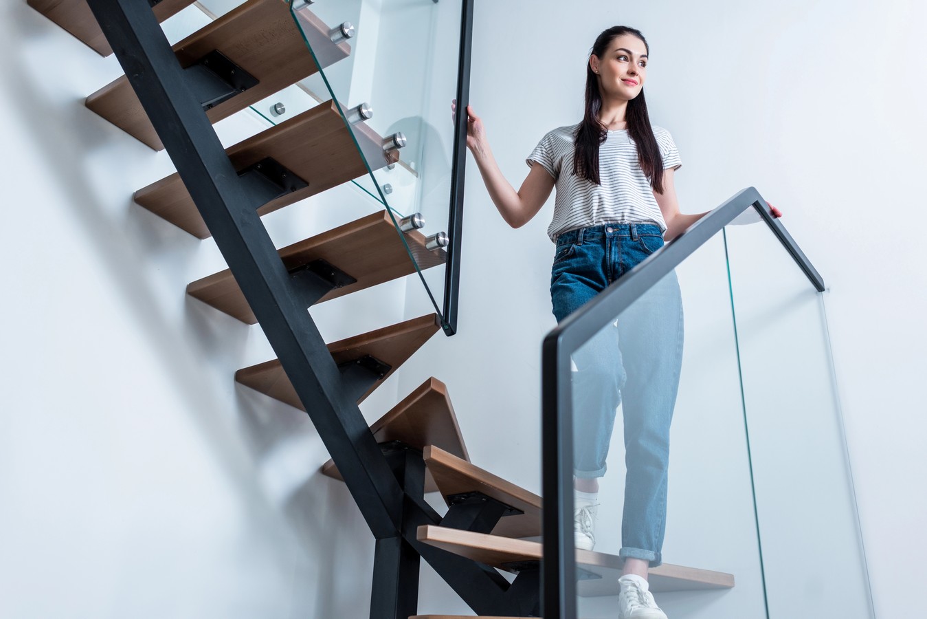 Woman on a steel stringer staircase with glass balustrade in a modern home